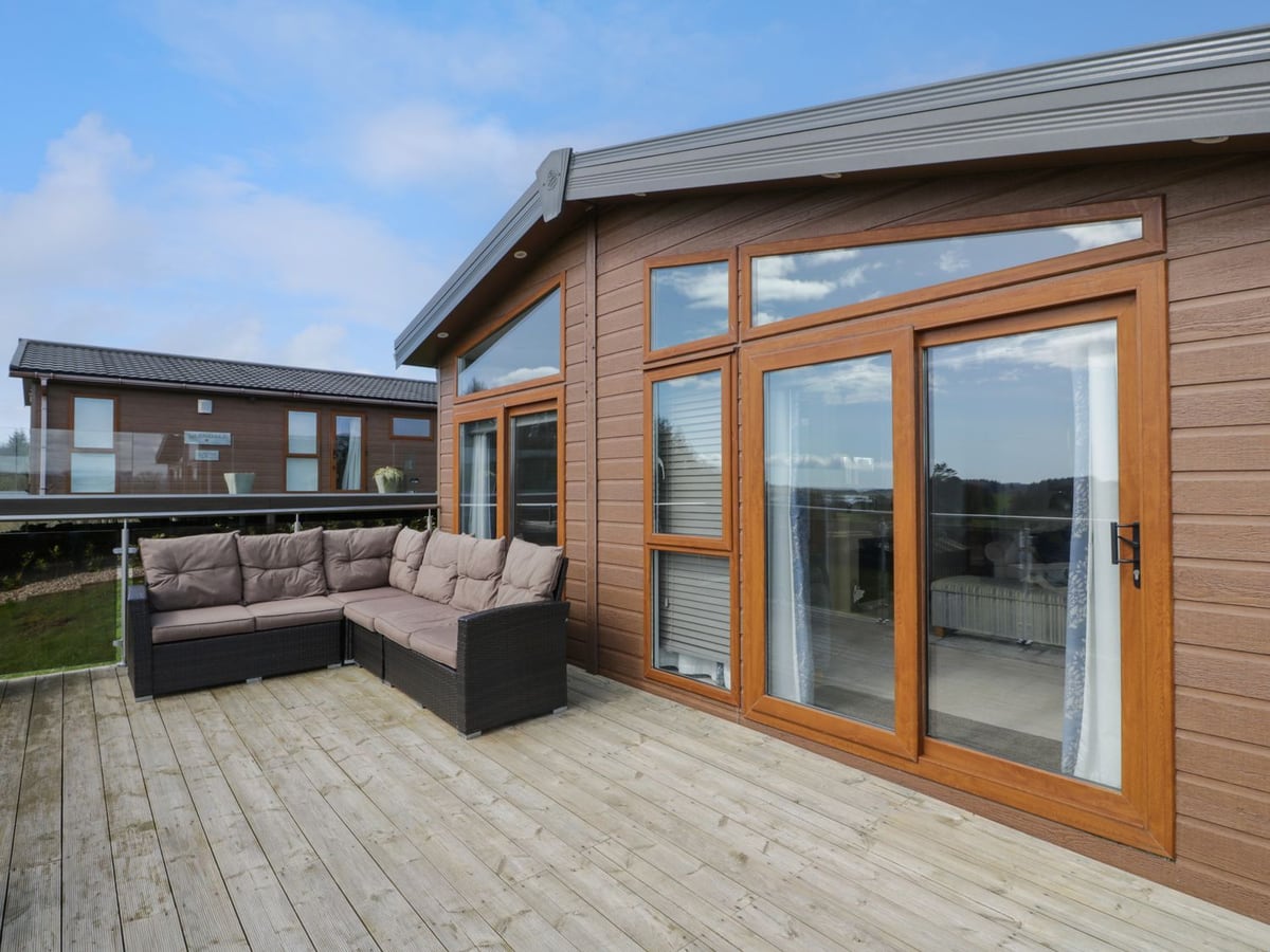 Outdoor sofa on the timber deck at 1 Fisherman's Hill, beside glazed doors and a neighbouring lodge