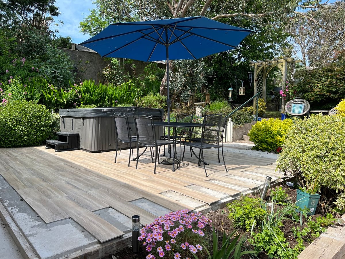 Covered hot tub and dining table under a blue parasol in the garden at 1 Gloucester Way