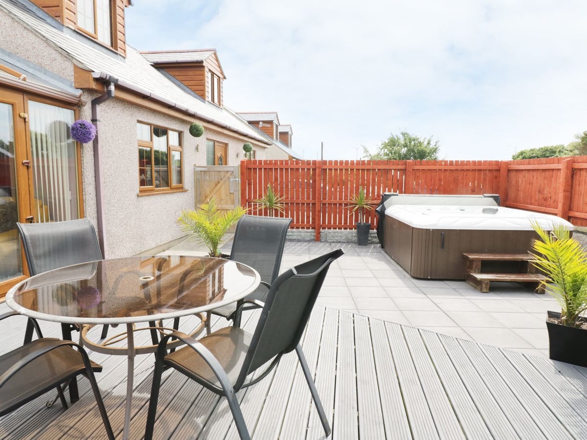 1 The Old Smithy decked patio with glass table and chairs, paved area and hot tub by a red timber fence