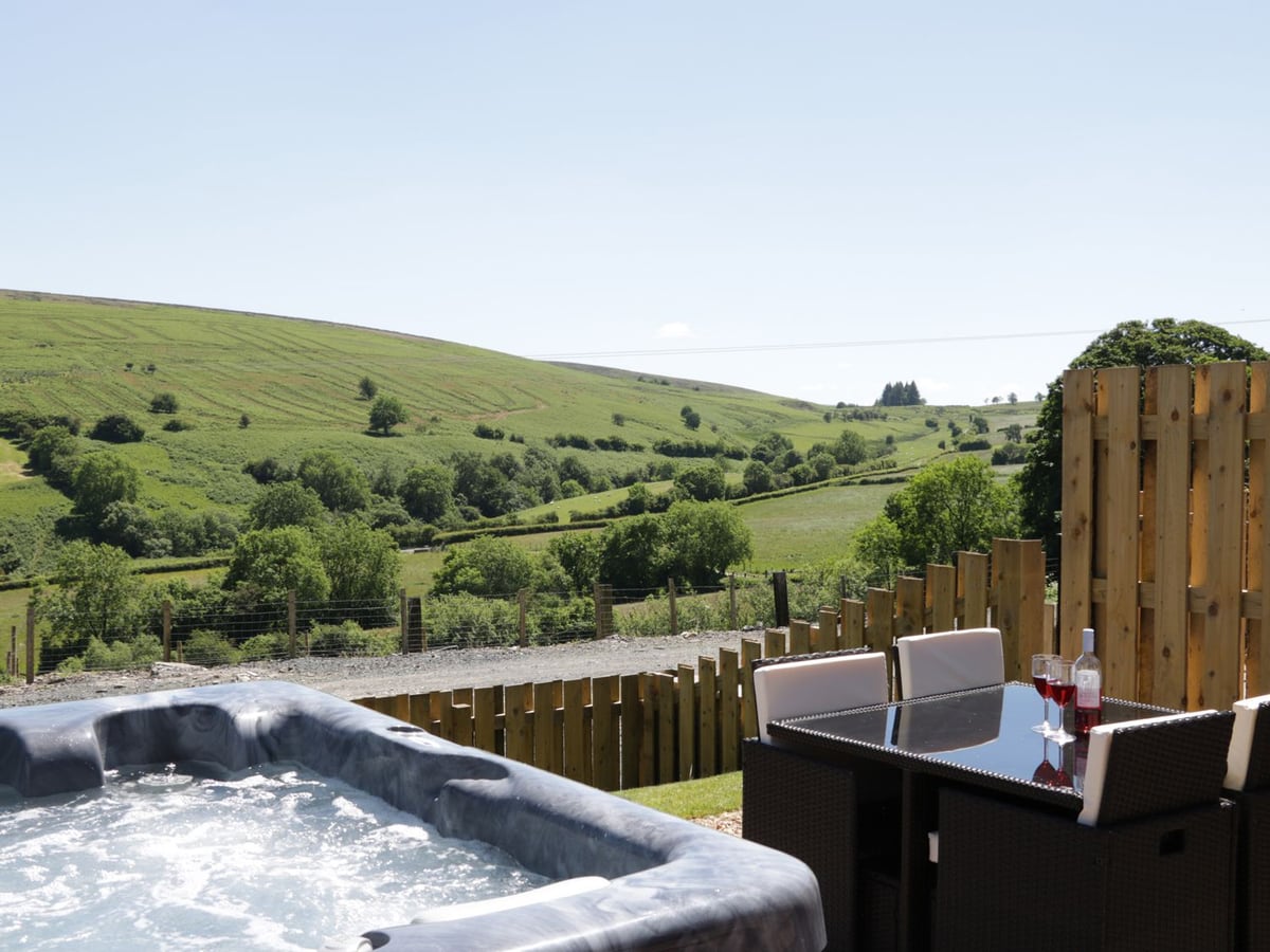 Hot tub and outdoor dining set behind a timber fence, with green valley views at 2 Beacon View Barn