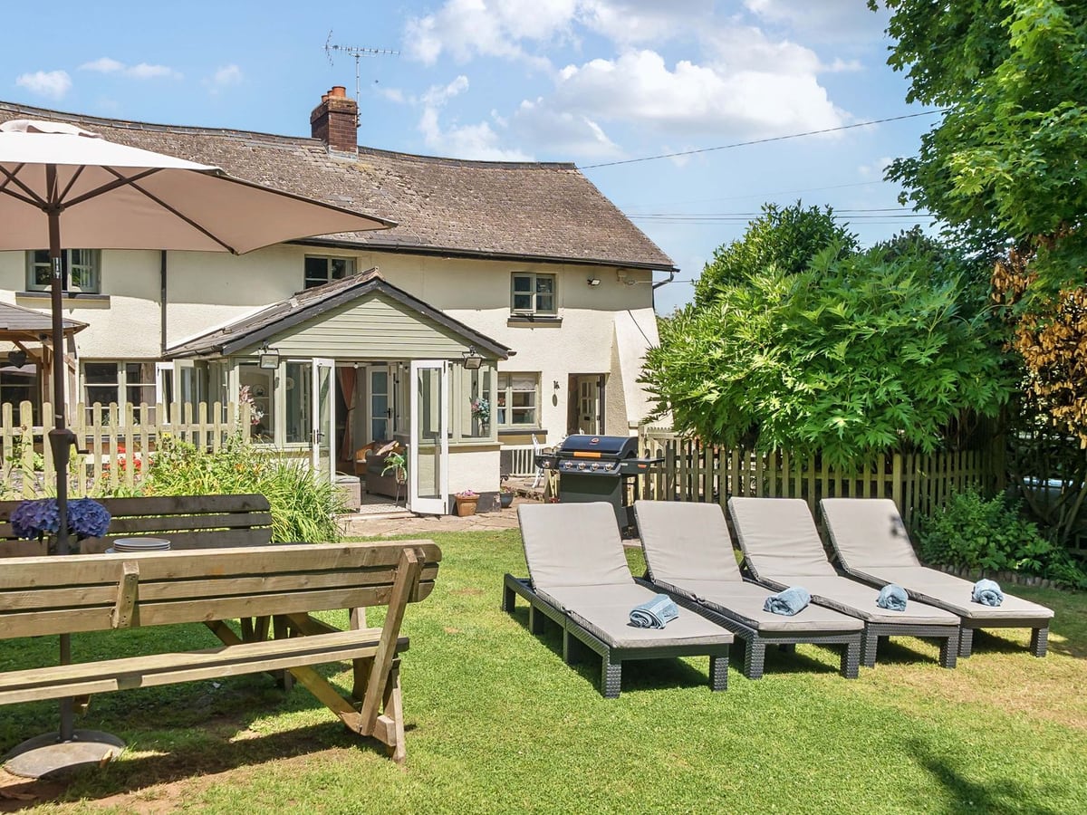 Cottage and conservatory behind garden furniture and loungers at 2 Pigsfoot Cottages
