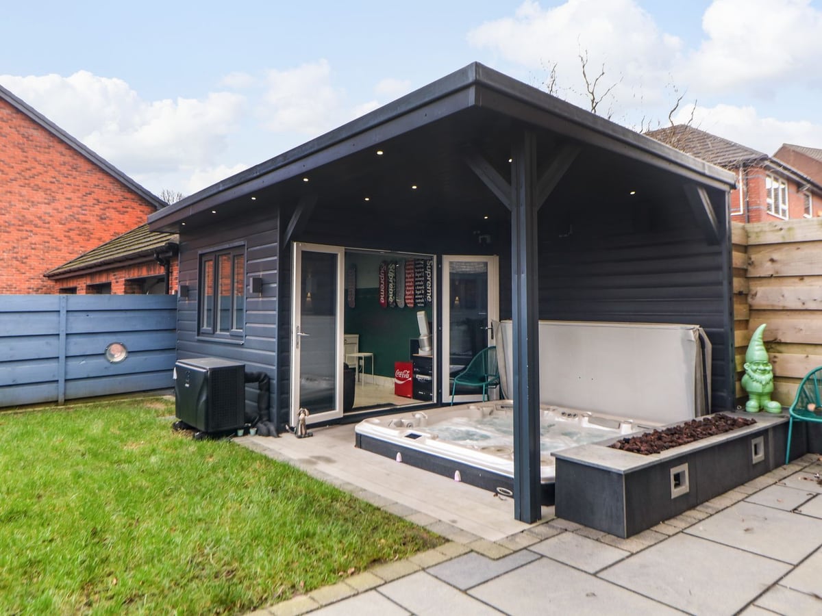 Hot tub beside the summerhouse and lawn with blue garden fencing at 4 Rockcliffe Grange