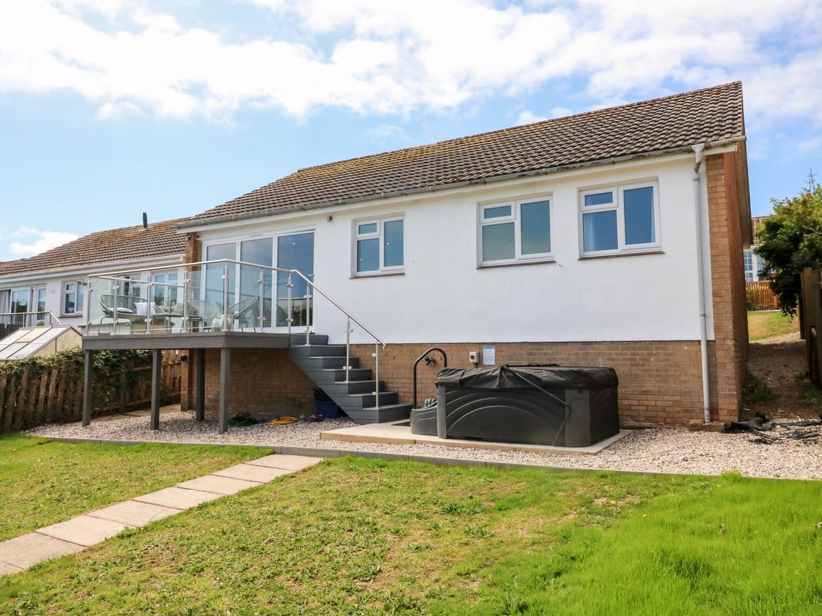 Rear elevation, raised balcony, steps and a covered hot tub beside the lawn at 65 Channel View