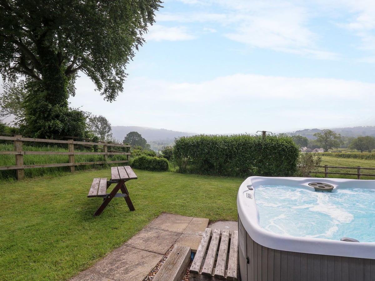 Aberdauddwr lawn with picnic bench and open hot tub beside a hedge and fields beyond