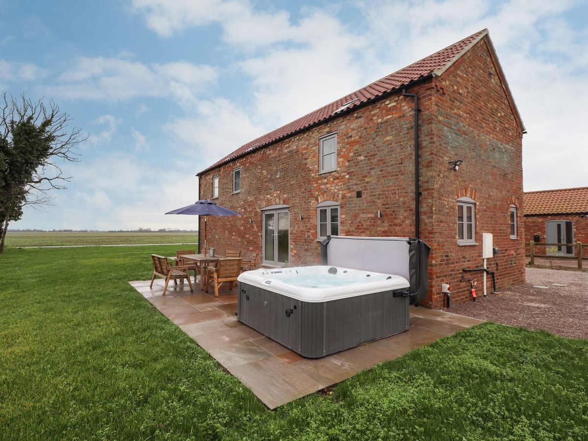 Brick Acacia Barn beside lawn and a patio with hot tub and dining table