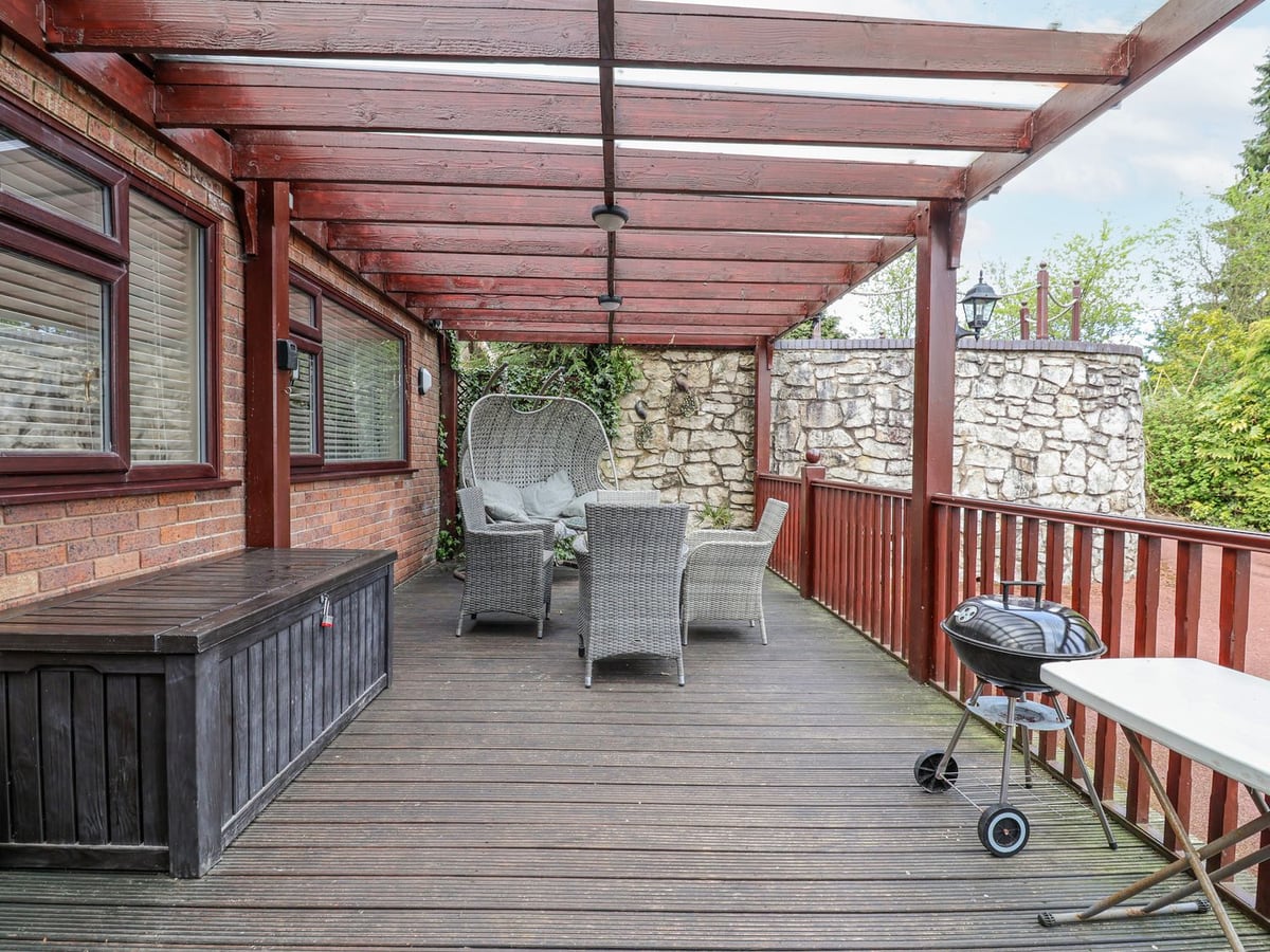 Covered timber deck at Acorns with rattan chairs, hanging egg chair, barbecue and a stone wall