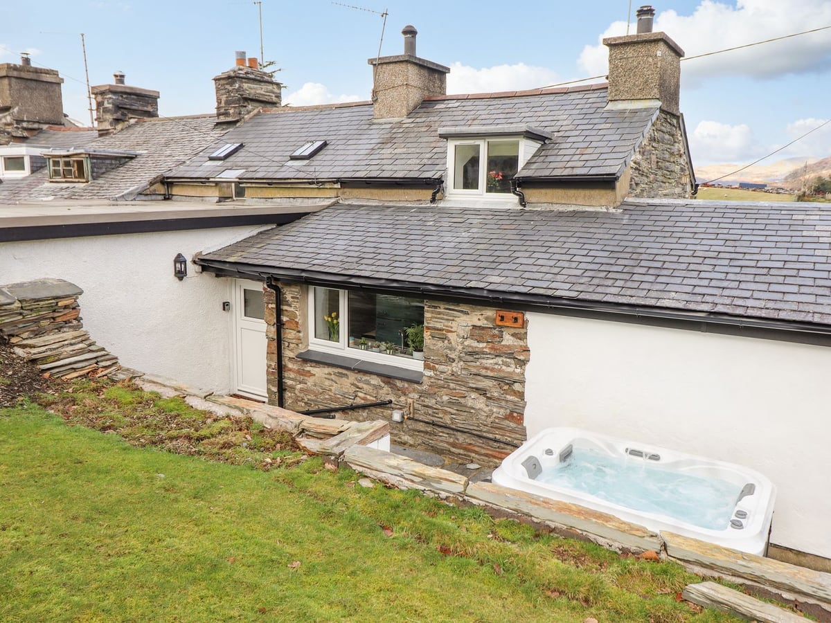 Rear of Ael Y Bryn cottage with a lawn above a hot tub set against the whitewashed wall