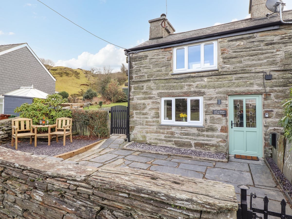 Ael Y Bryn cottage exterior with patio seating, garden gate, and hills beyond
