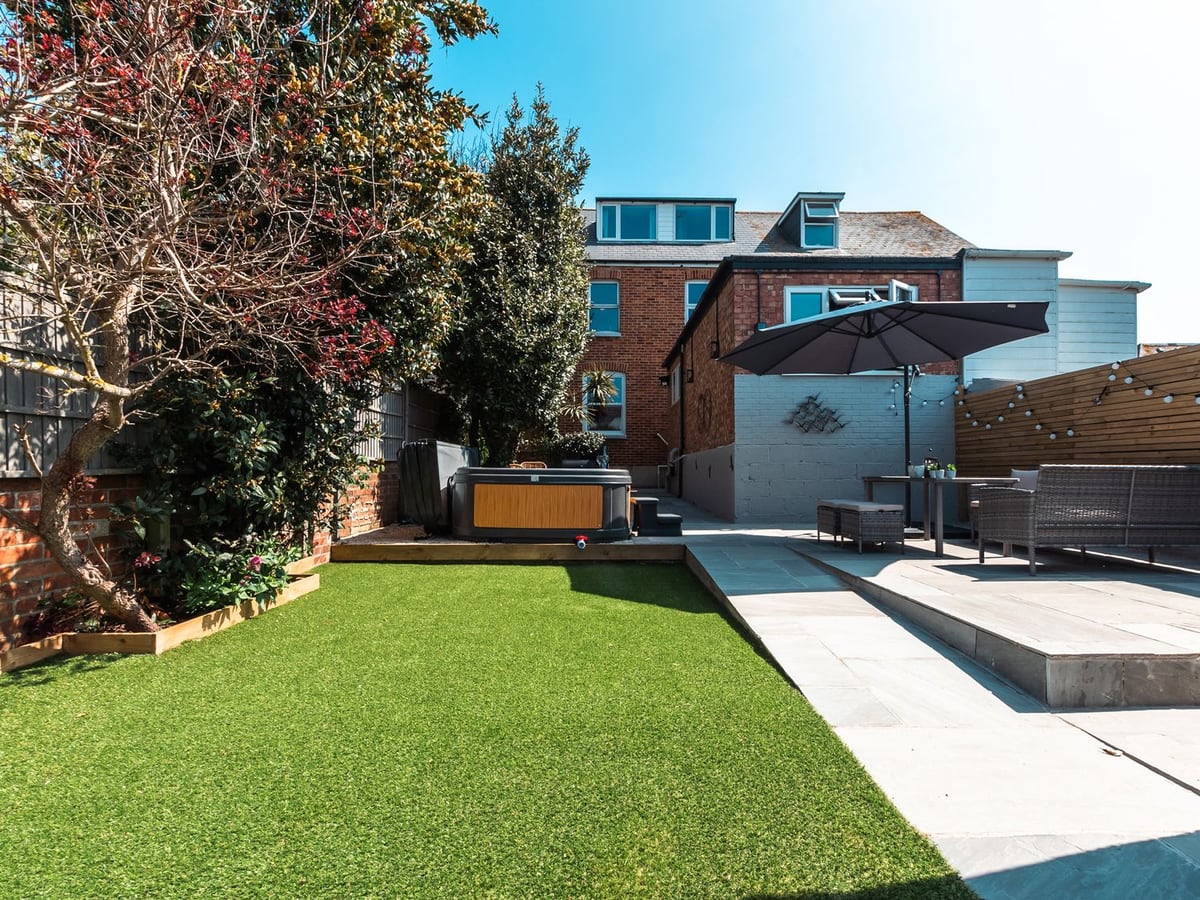 Anchor House behind an artificial-grass garden, with a hot tub and a raised seating terrace