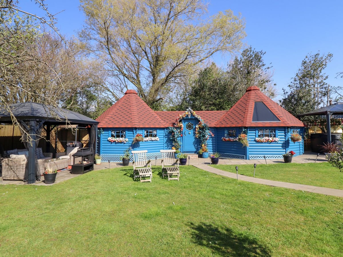Applejacks Orchard blue timber cabin with a lawn, two wooden loungers and a gazebo seating area