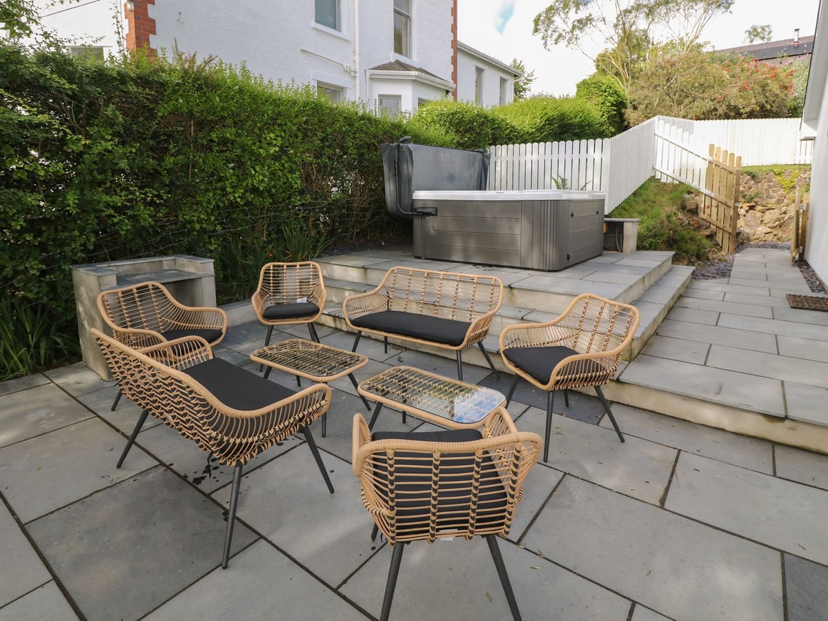 Paved patio at Argraig with rattan seating, a raised hot tub, hedging and white picket fencing