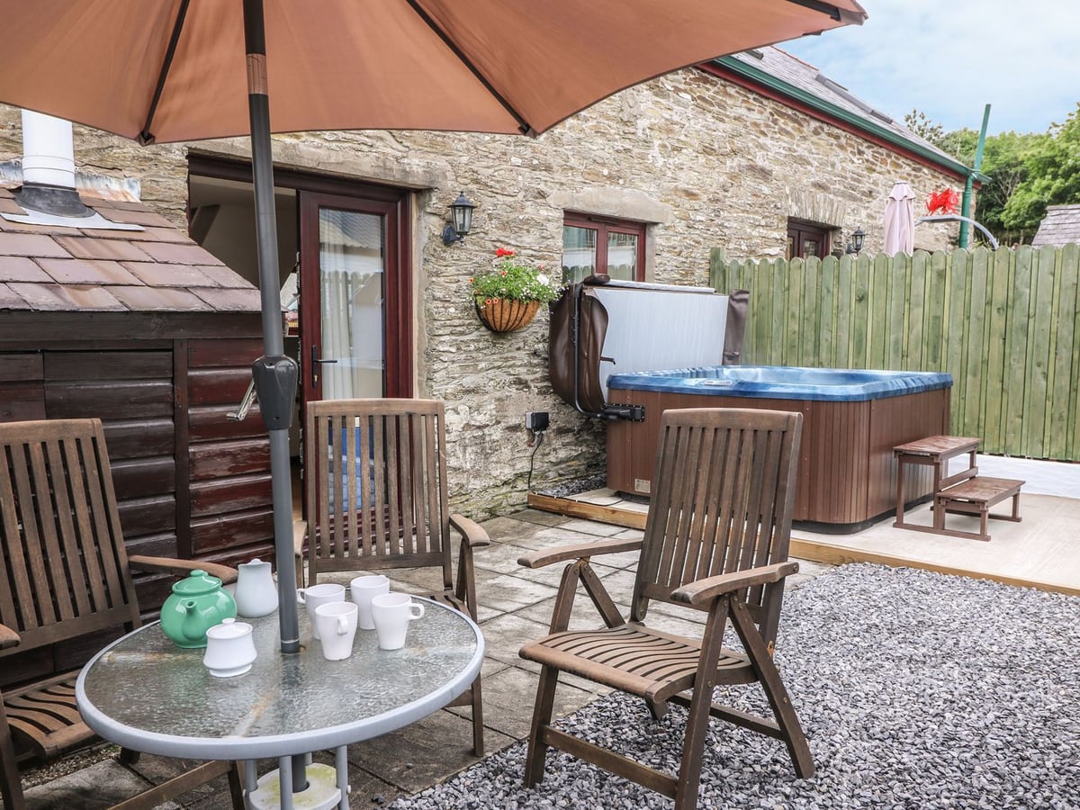 Ash Cottage patio with table and chairs under a parasol, hot tub with its lid raised and a timber fence
