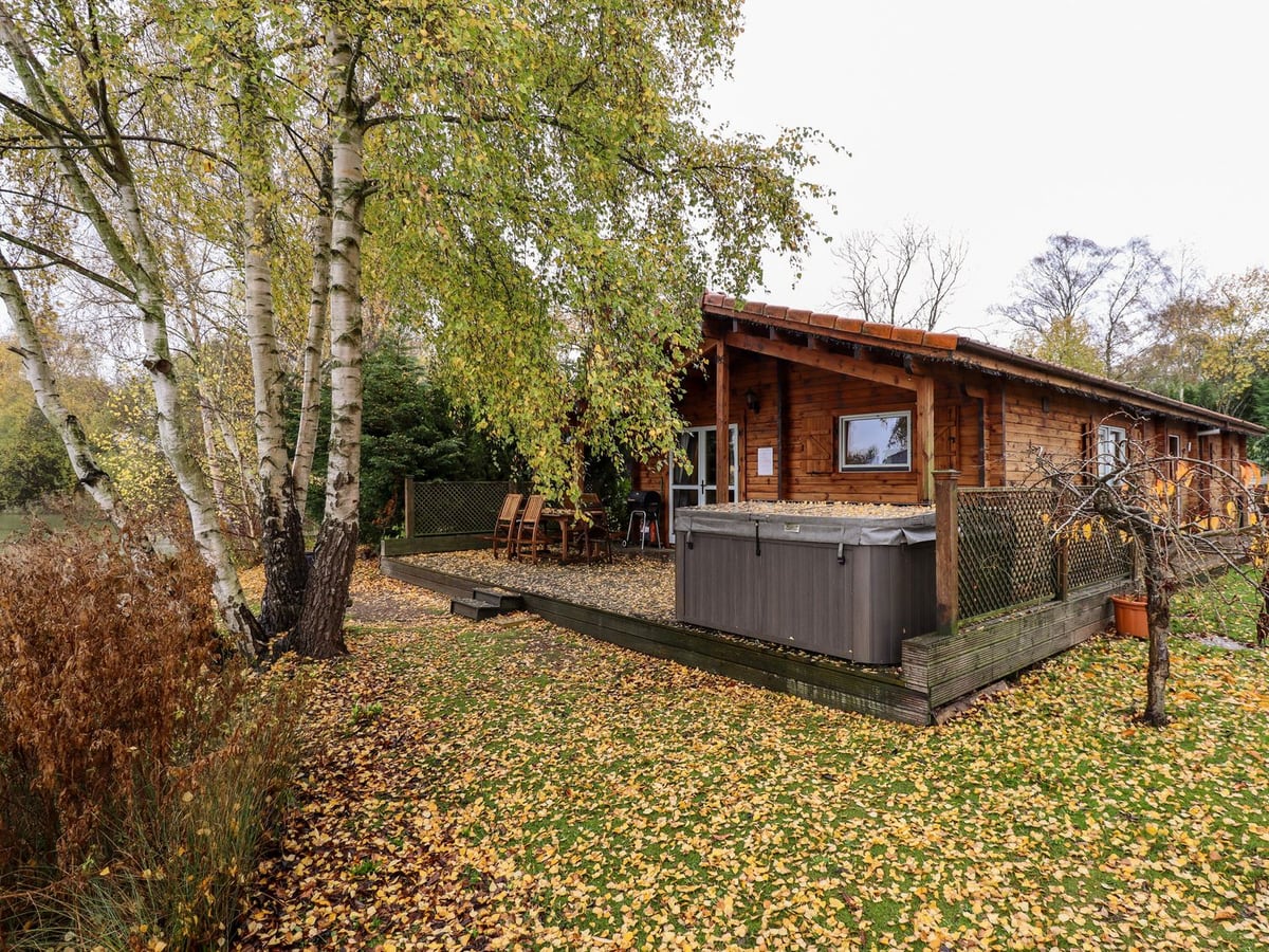 Avocet Lodge's timber exterior and hot tub deck beside trees and a lawn