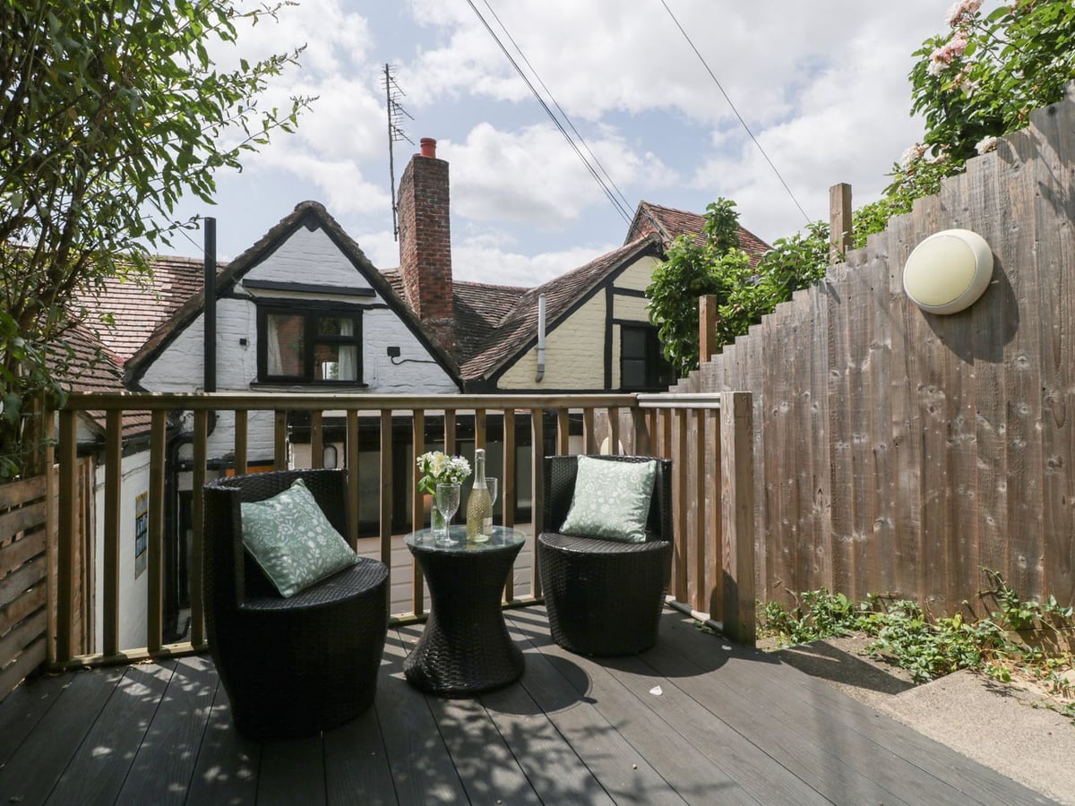 Two chairs and a small table on Avonmede decking, with a wooden railing and cottage roofs beyond