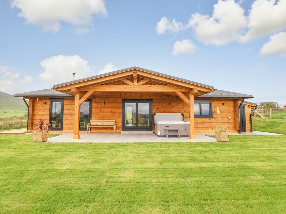 Bacheiddon Log Cabin with a hot tub and bench under a timber canopy, set behind a mown lawn