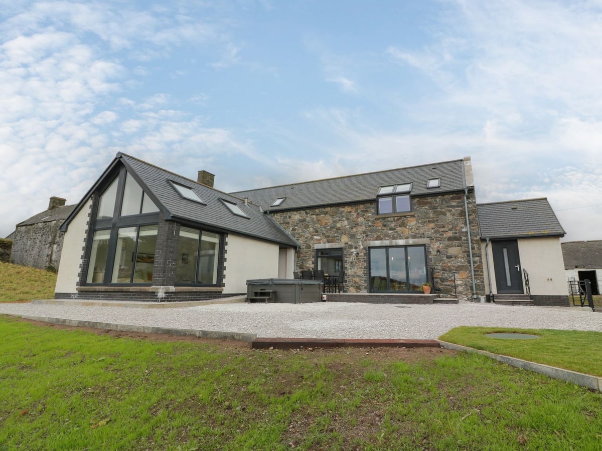 Balcarry Barn stone exterior with a glazed gable, hot tub and gravel terrace above the lawn