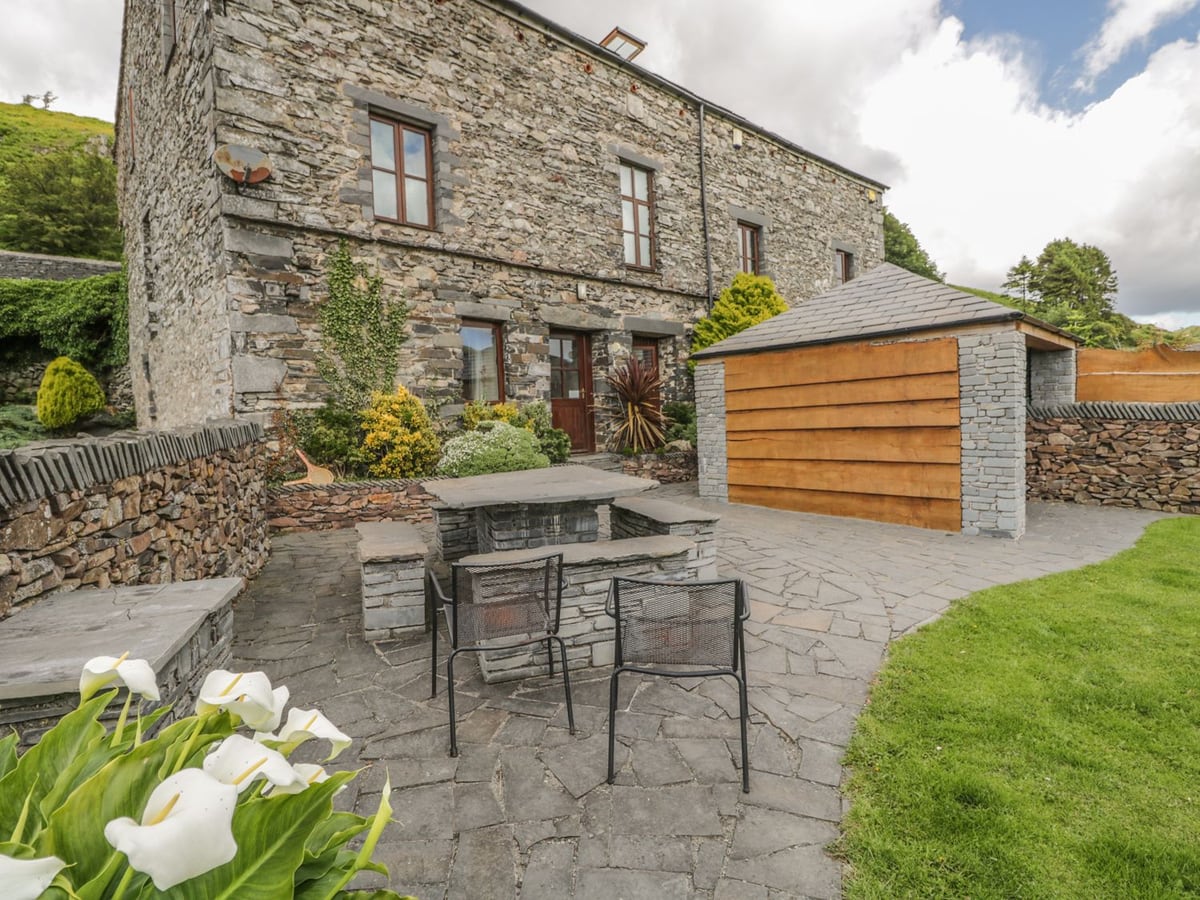 Bank End Barn stone exterior with a paved seating area, lawn and timber hot tub shelter