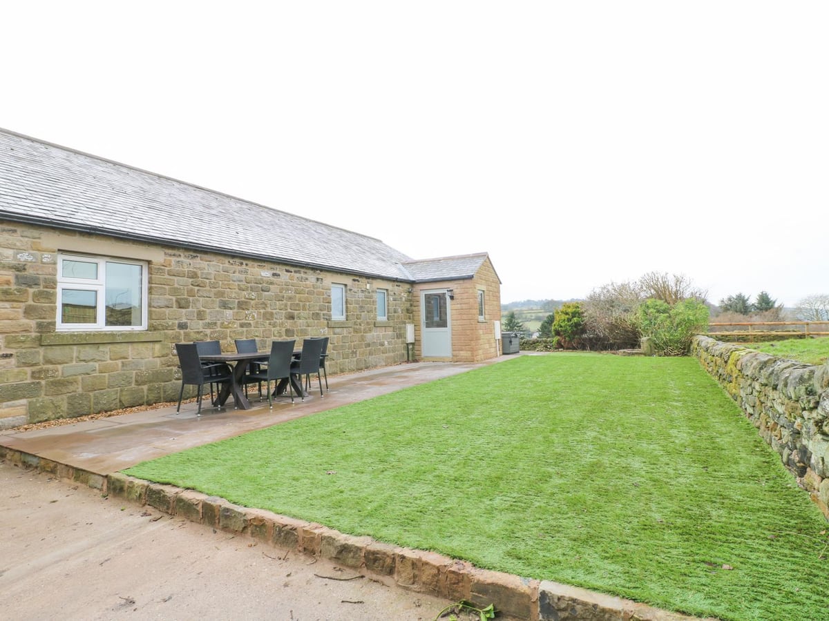 Stone walls, patio table and a long lawn beside the single-storey building at Barncroft