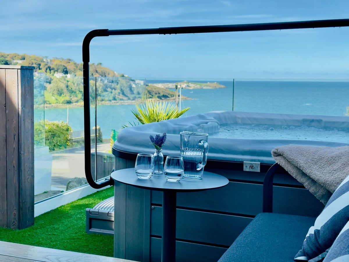 Bayvista's hot tub and terrace seating behind a glass balustrade, overlooking the blue sea