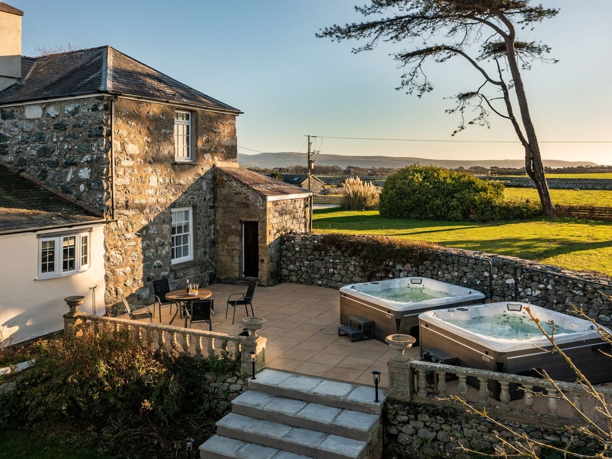 Bennar Fawr stone house with two open hot tubs on a balustraded patio, steps and lawn beyond a wall