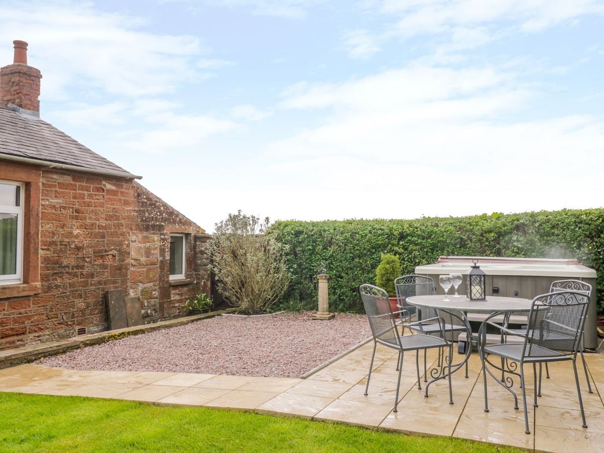 Lawn and paved seating area beside the stone walls and hot tub at Berrymoor Cottage