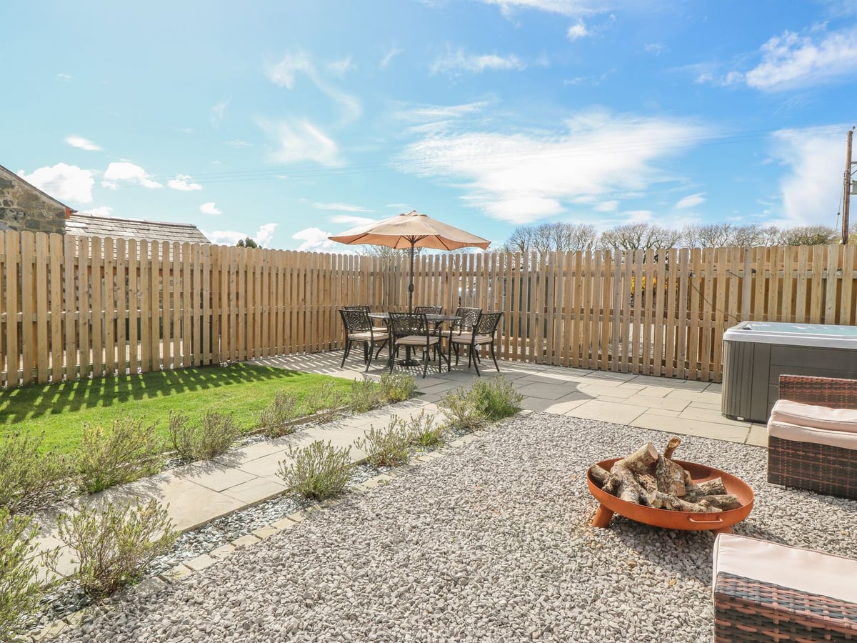 Beudy garden with wooden fencing, lawn, patio dining table, fire pit and part of a hot tub
