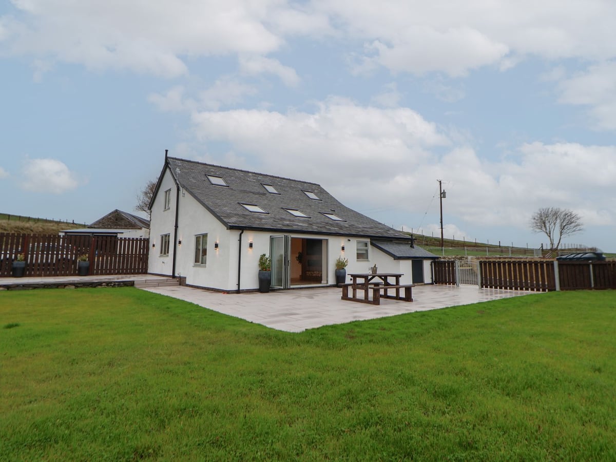 Beudy Pwll Pridd white cottage with paved patio, picnic bench, wooden fencing and a wide lawn