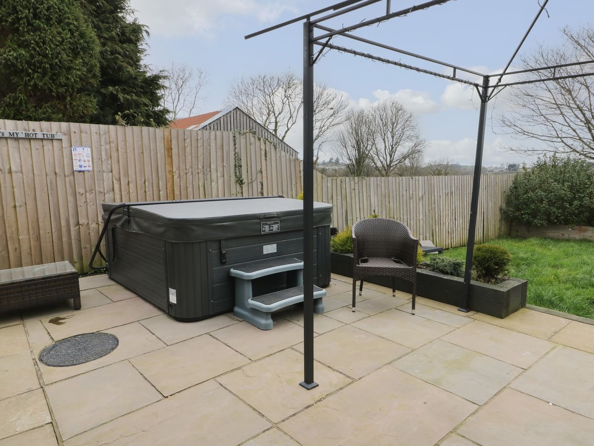 Big Azzles patio by timber fencing, with a hot tub with its lid on, a wicker chair and a lawn
