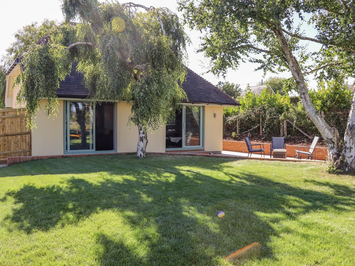 Birch Cottage opening onto a lawn with birch trees and a paved seating area beside the house