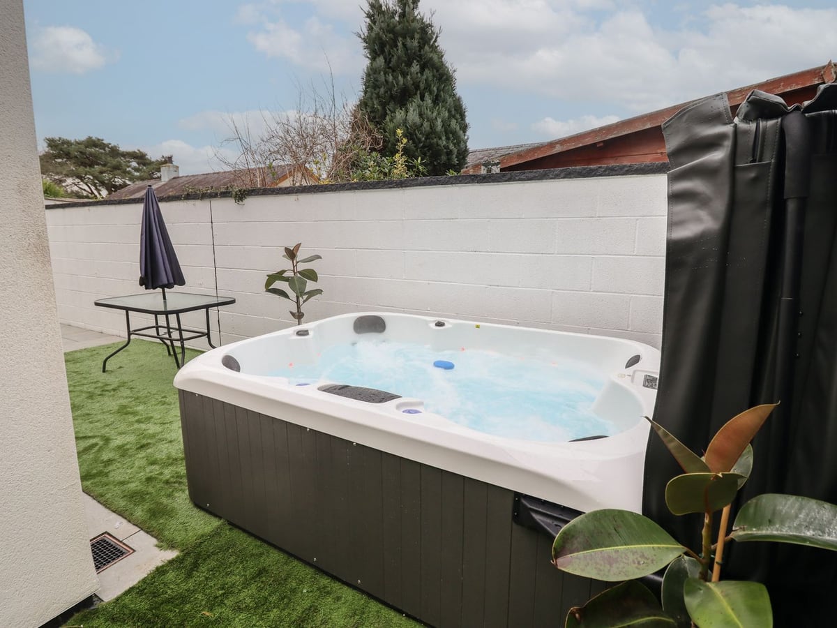 Hot tub on artificial turf beside a white block wall at Blackrock Gem, with a glass table and parasol