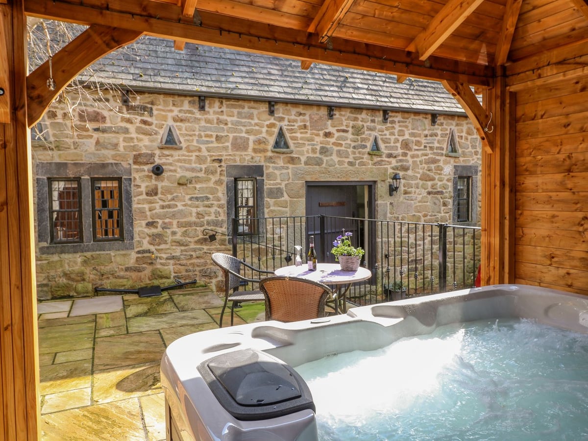 Covered hot tub and patio table facing the stone doorway and windows of Bluebell Cottage