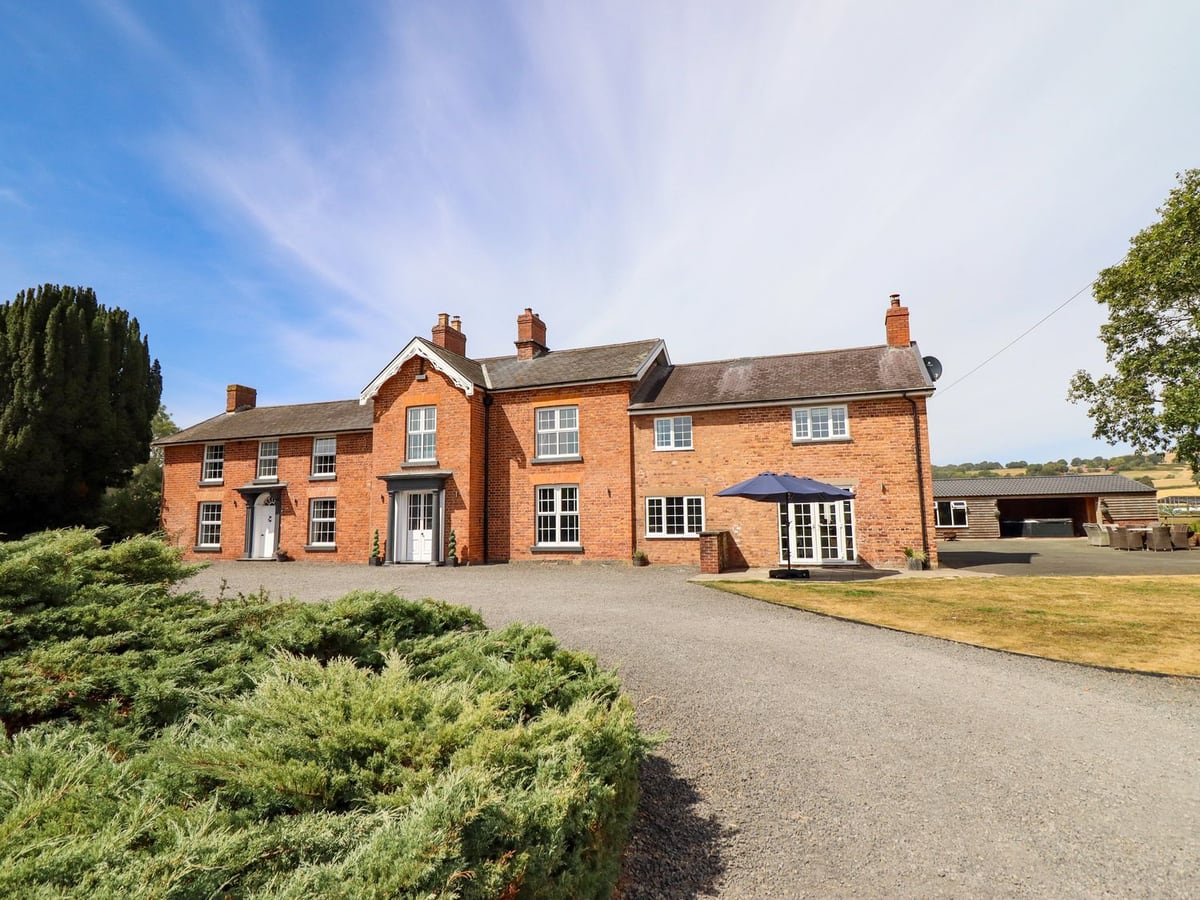 Bodaioch Hall, a large red-brick house with a gravel drive, lawn, patio parasol and open-fronted outbuilding