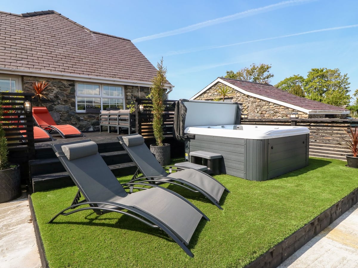 Bodrual Cottage hot tub and two loungers on artificial grass beside a raised deck and stone cottage