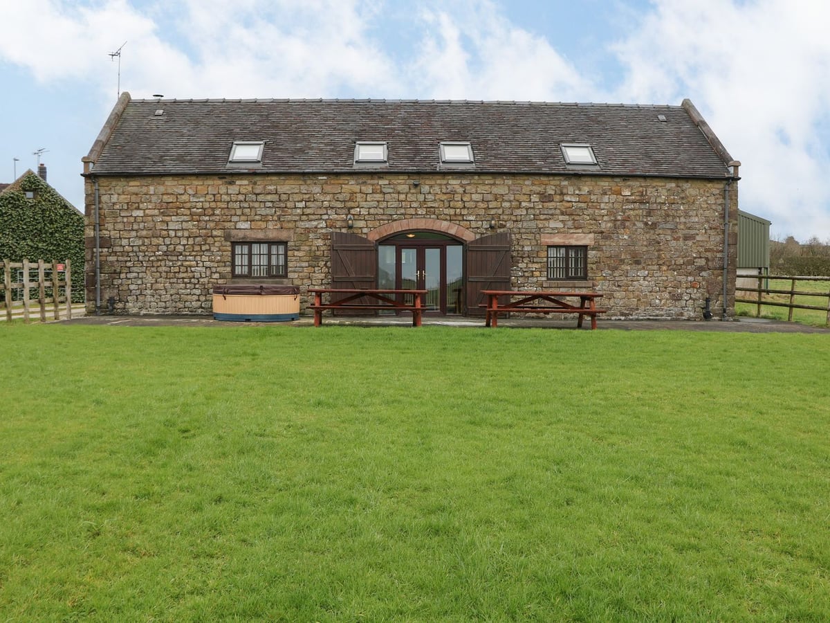 Stone exterior of Bottomhouse Barn with a broad lawn, picnic tables and a covered hot tub.
