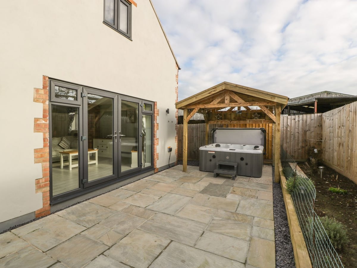 Bramley Cottage rear patio with a covered hot tub beside the house exterior