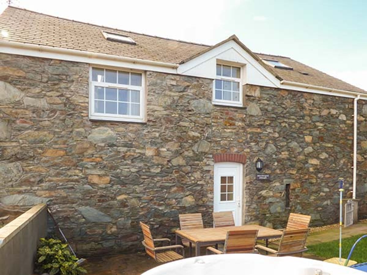 Bran Goesgoch stone barn exterior with a wooden garden table and the edge of a hot tub