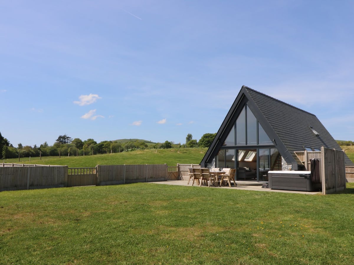 Brecknock Cheviot A-frame with a patio dining set and hot tub beside a large lawn edged by fencing