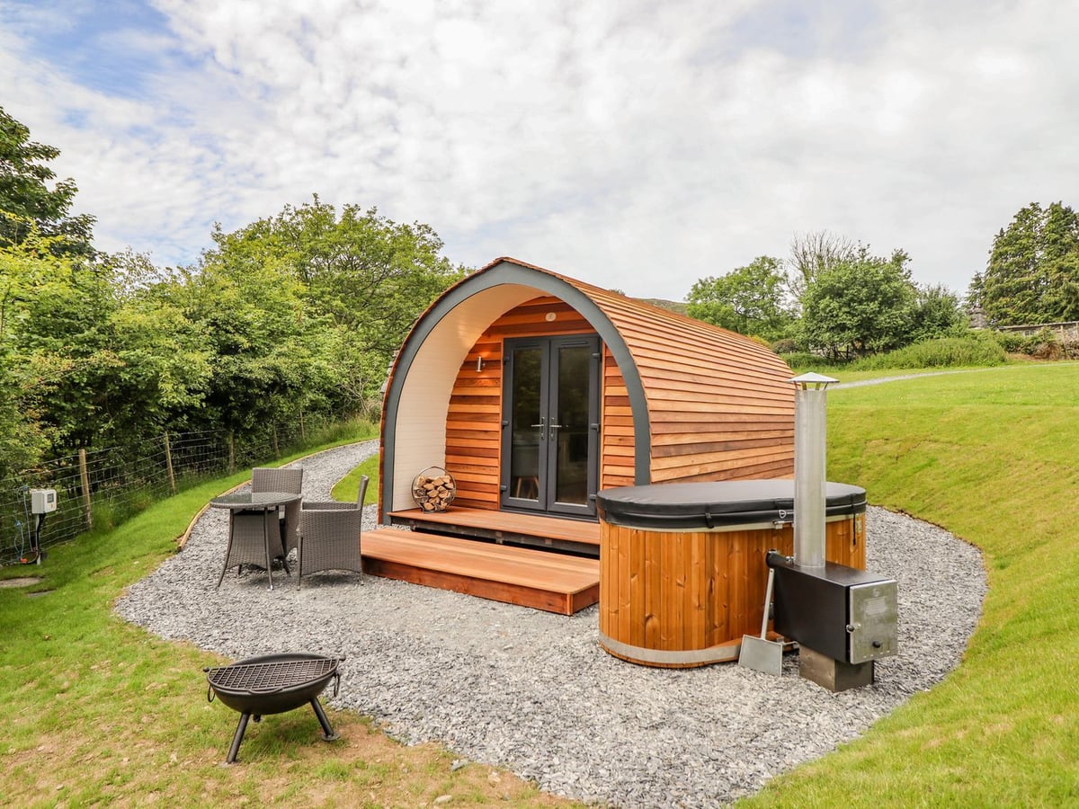 Briallen arched timber pod with a wood-fired hot tub with its lid on, patio set and fire pit on gravel