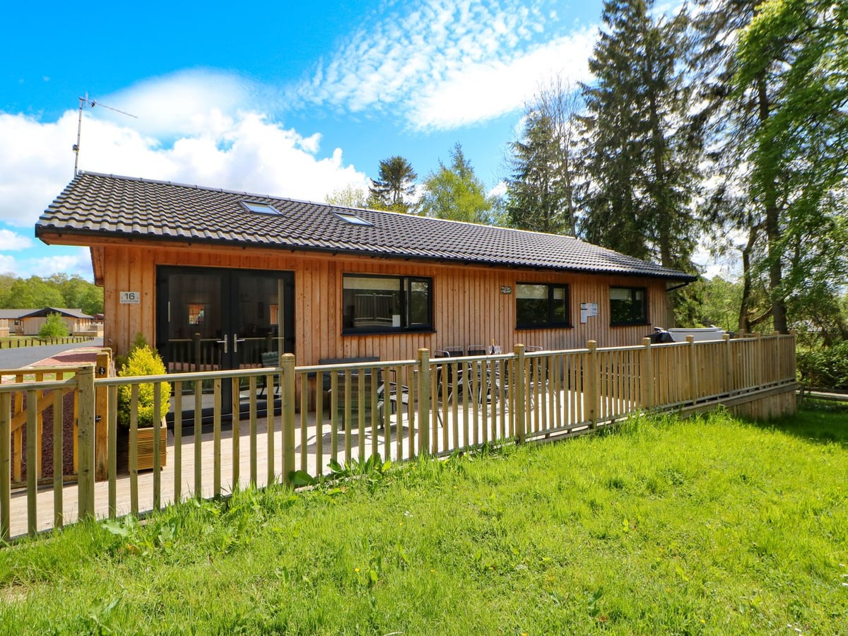 Timber exterior and railed deck at Broken-Sky Lodge, with grass and tall trees alongside.