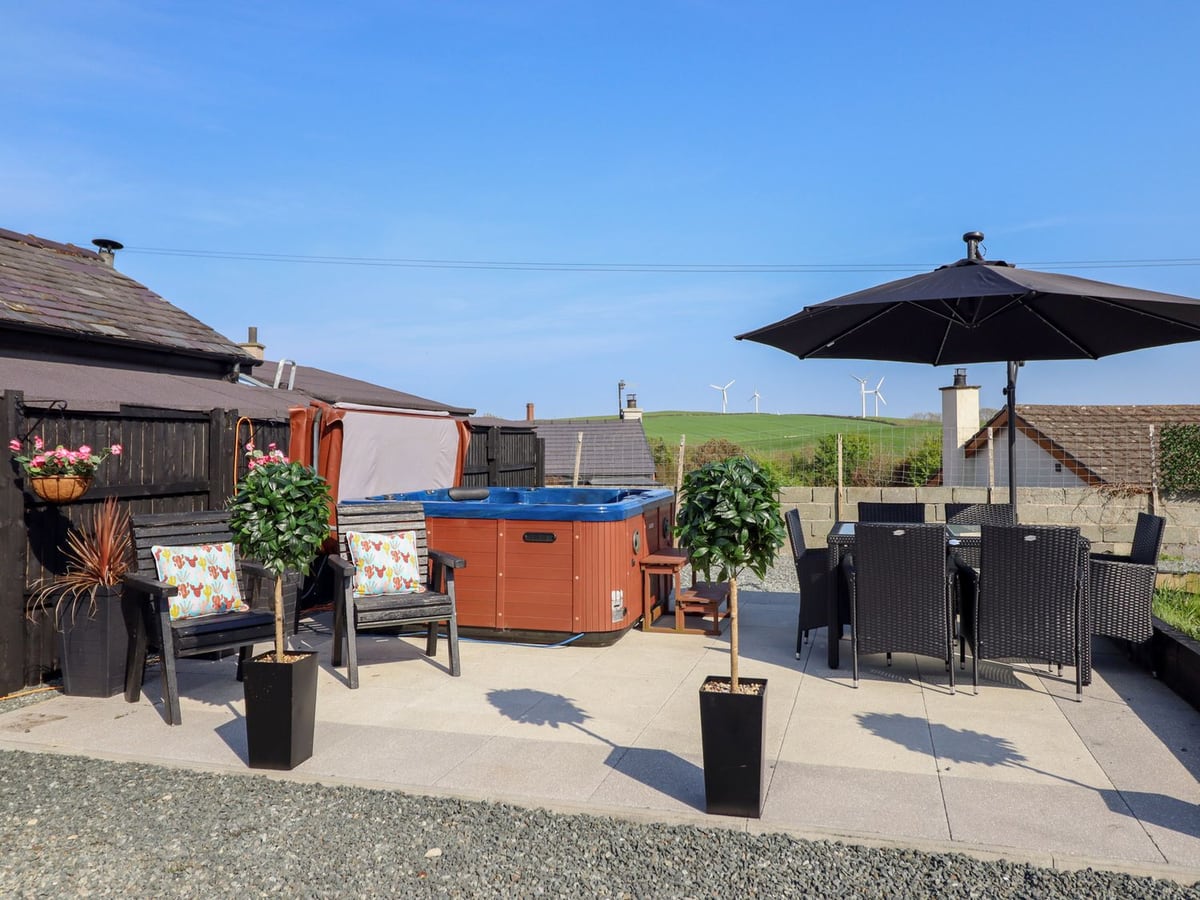 Bronallt gravel garden with a hot tub, patio dining table, parasol and outdoor chairs