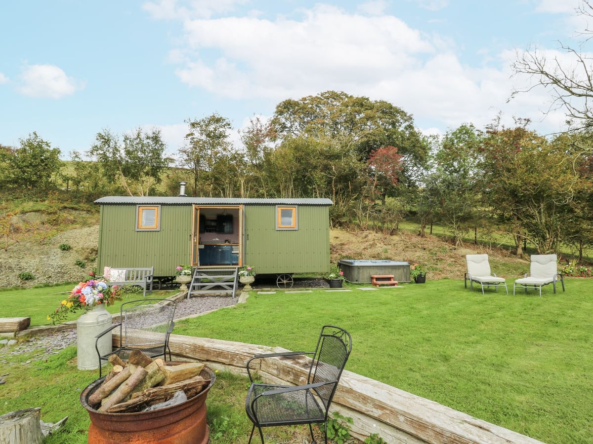 Brondel green shepherd's hut on a lawn with an open hot tub, sun loungers and a fire pit