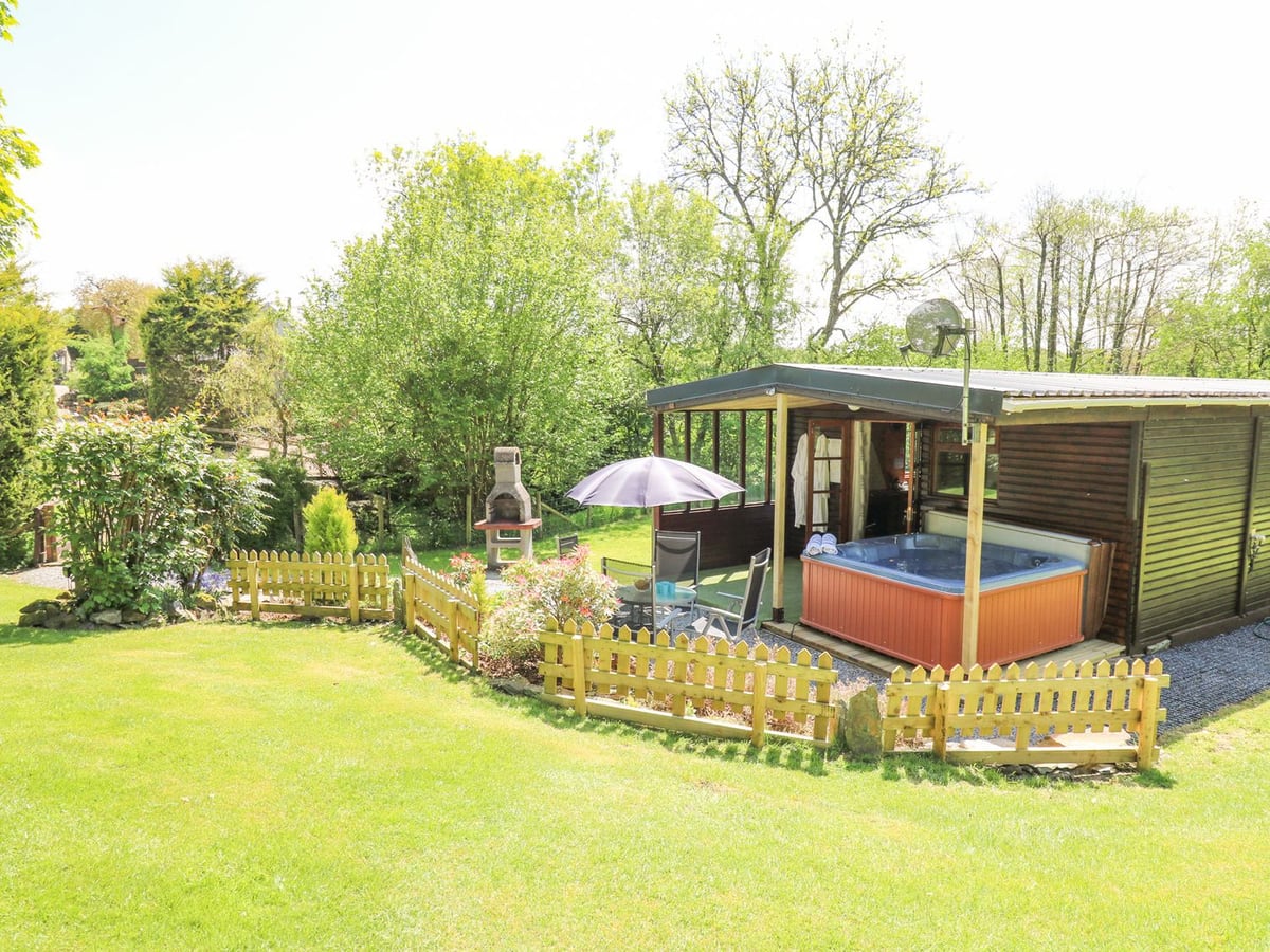 Brook Lodge timber lodge with a hot tub under the veranda, patio seating and picket fence by a lawn