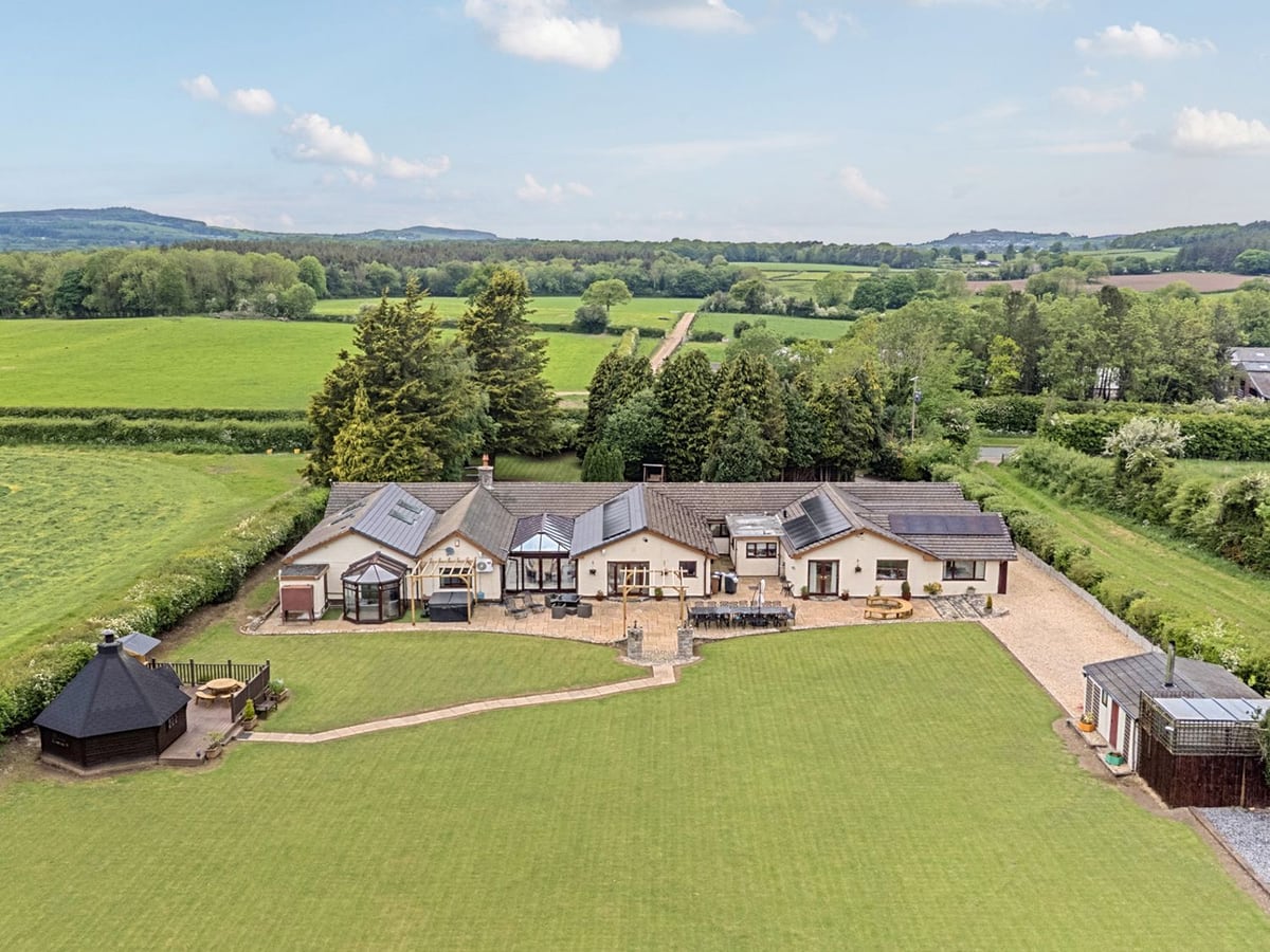 Aerial view of Brookway Lodge, a long bungalow with a patio, large lawn, BBQ hut and hedged fields