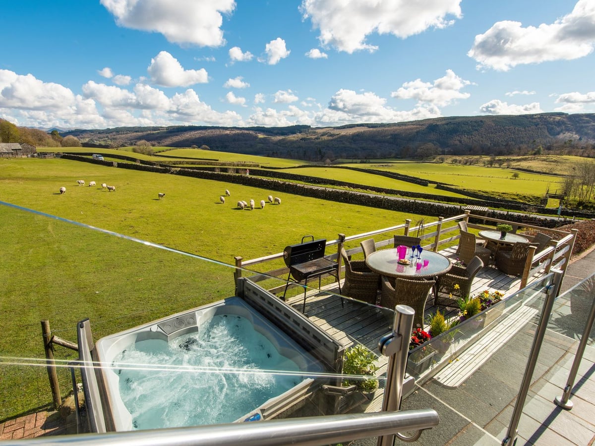 Browside hot tub and dining deck overlooking fields of sheep beyond glass and wooden rails