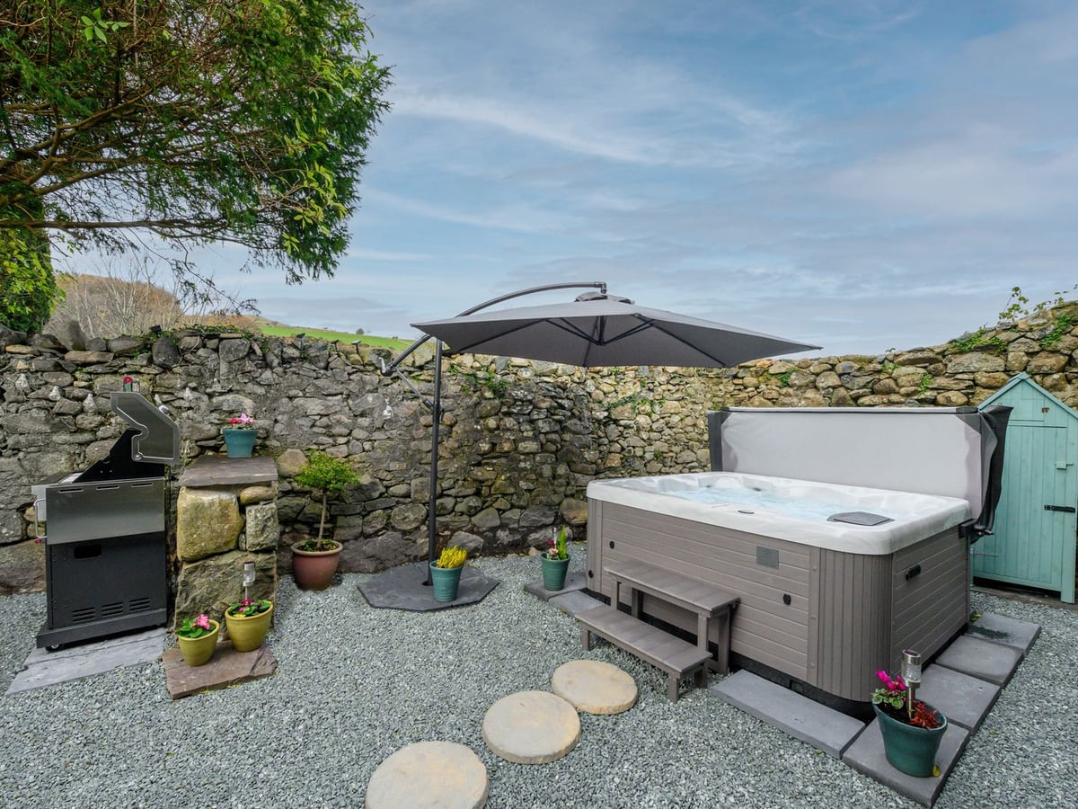 Bryn Aber Bach stone-walled gravel rear garden with a hot tub, parasol, barbecue and small shed