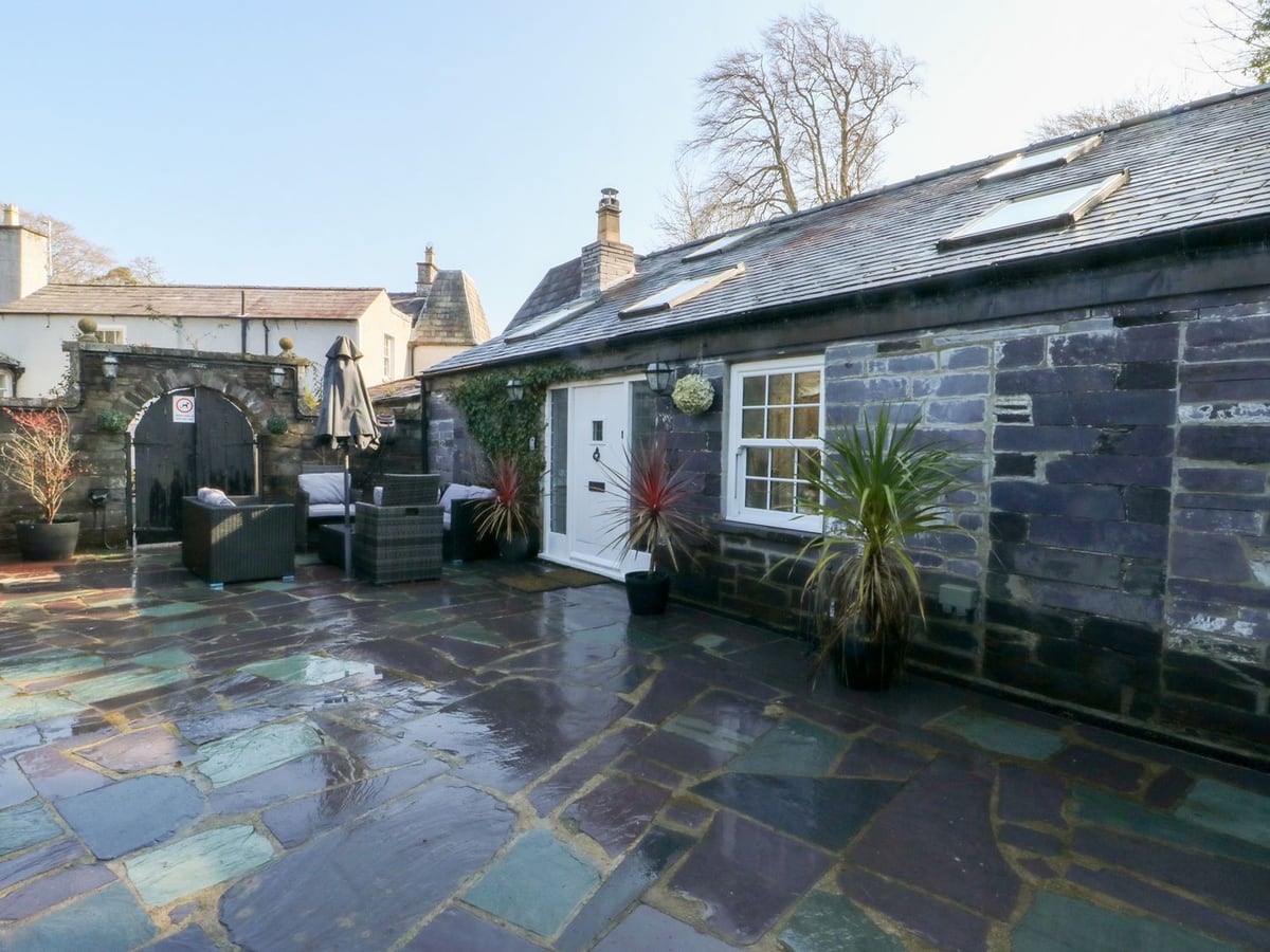 Bryn Derwen Coach House slate cottage with a paved courtyard, rattan seating and an arched wooden gate