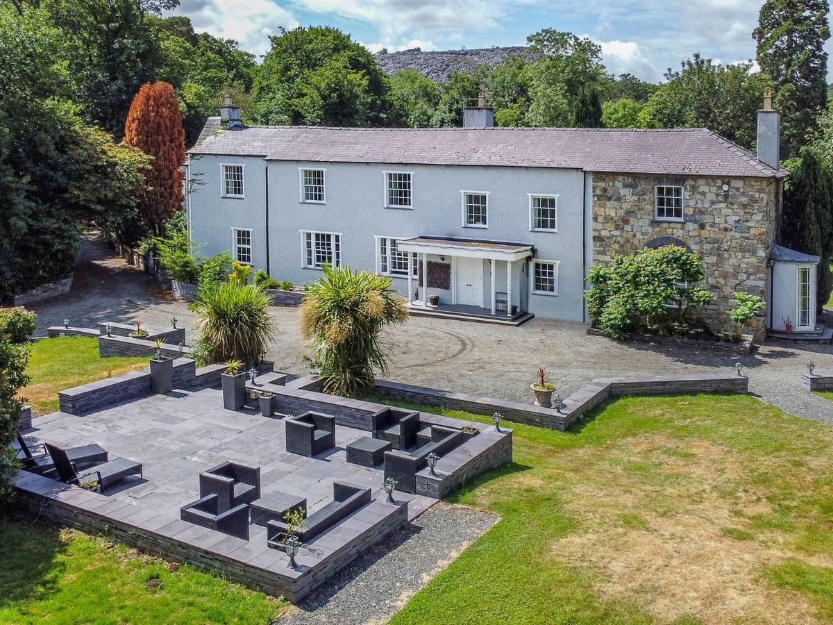 Bryn Derwen, a large white-rendered and stone house with a slate terrace, outdoor seating and lawns
