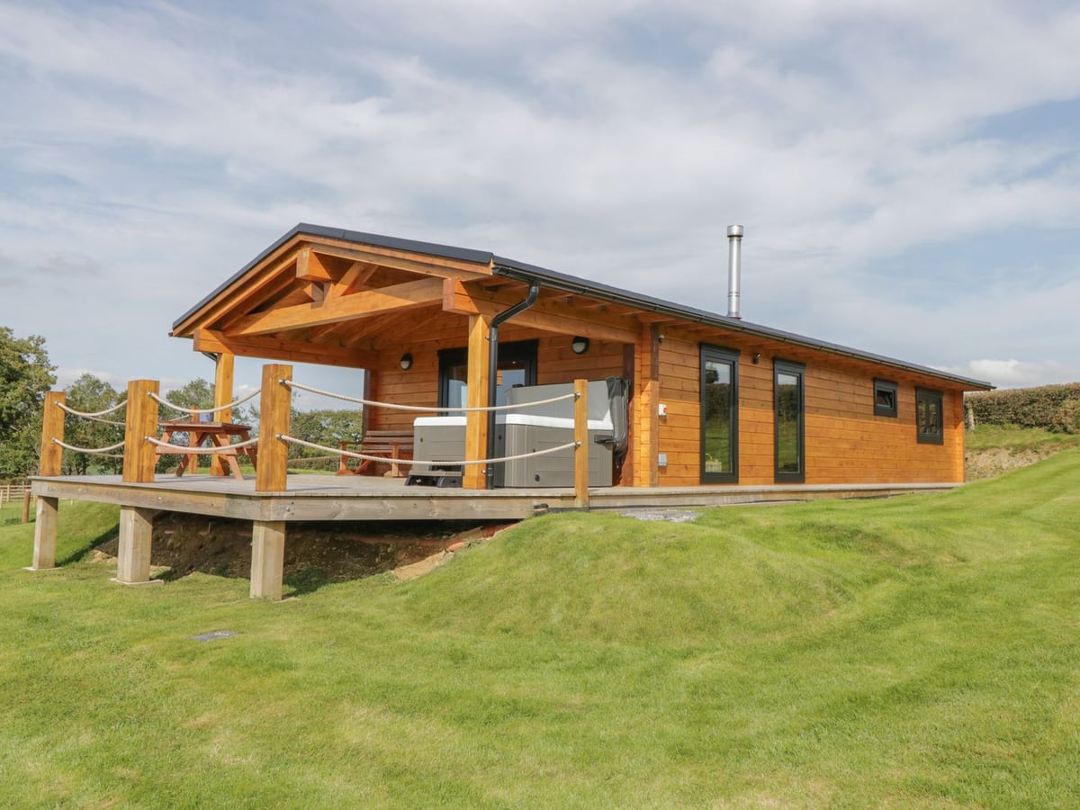 Bryn Eiddon Log Cabin with a covered raised deck, rope rails, hot tub and surrounding lawn