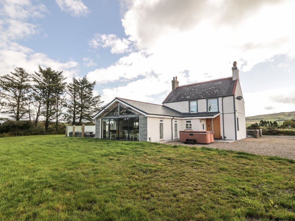 Bryn Ffynnon white house with a glazed extension, a large lawn and a hot tub with its lid on by gravel