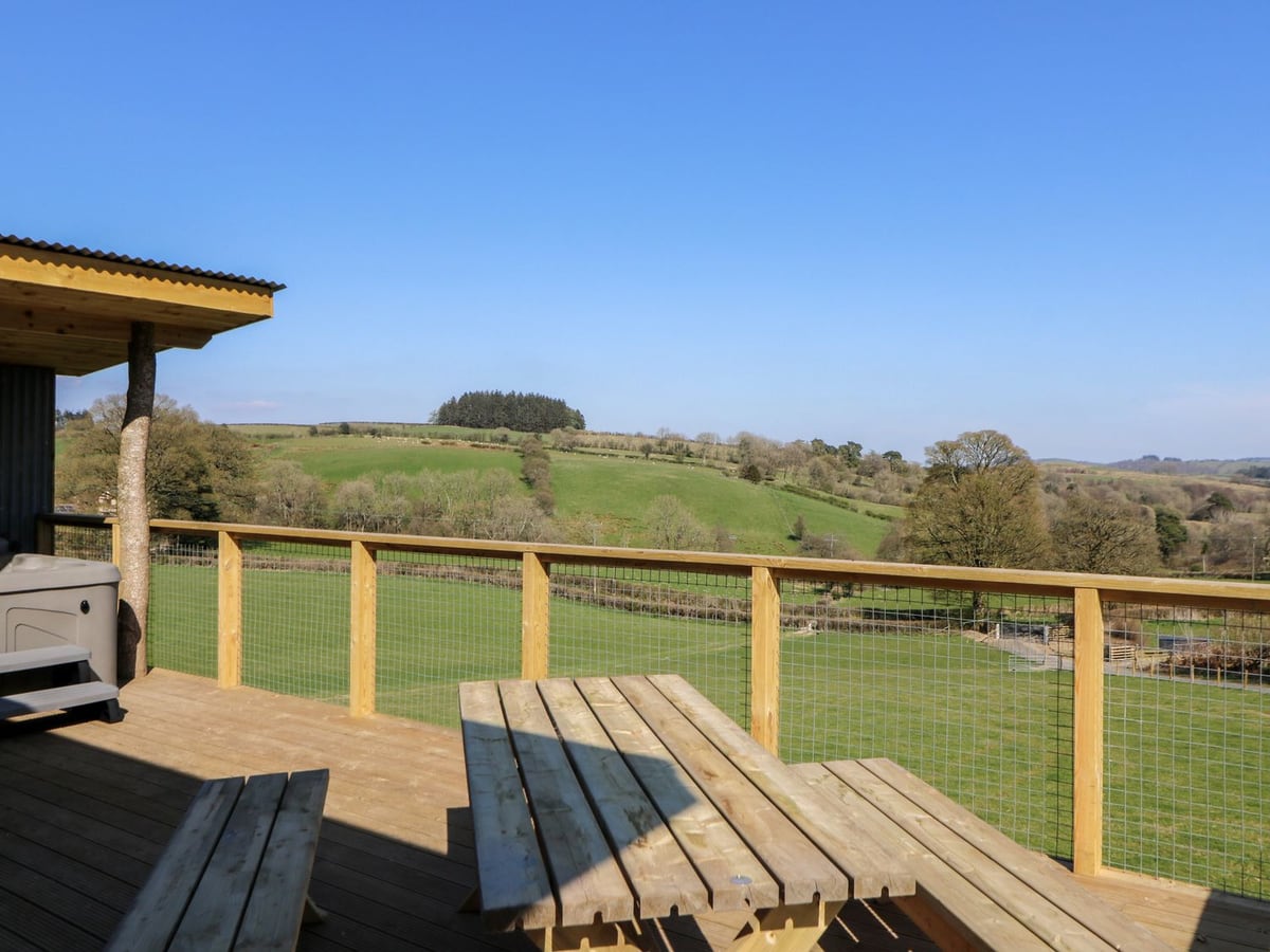 Bryn Hafod raised decking with a picnic table, mesh railings, a hot tub corner and green fields beyond